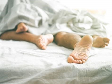 partners showing their feet on bed with sheets